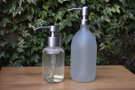A clear glass Kuishi soap dispenser and a matt white glass Kuishi soap dispenser on a table